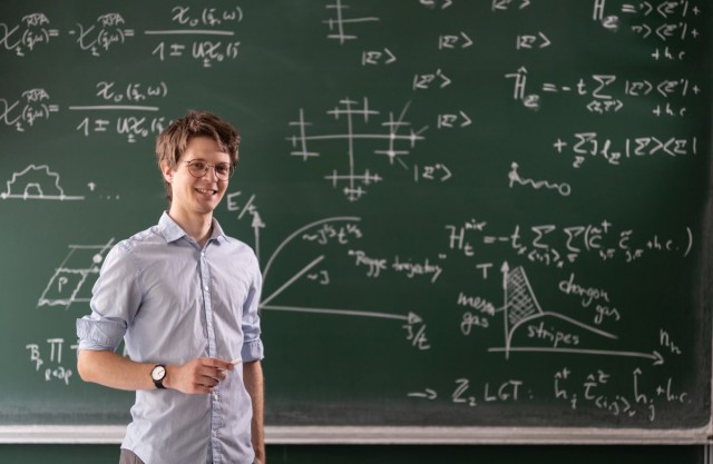 Fabian Grusdt standing in front of a blackboard filled with formulas.