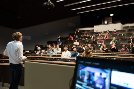 Professor giving a welcome talk in front of students in an auditorium. 