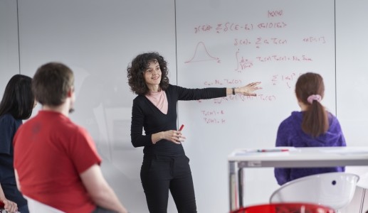 Theory PhD students attending a meeting with senior researcher, discussing formulas on a whiteboard.