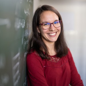 Female scientist leaning on a blackdoard filled with mathematical formulas.