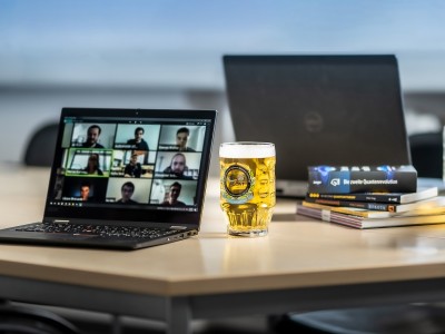 Open laptop with a zoom call on a wooded table with a full bier mug nearby and quantum physics books. 