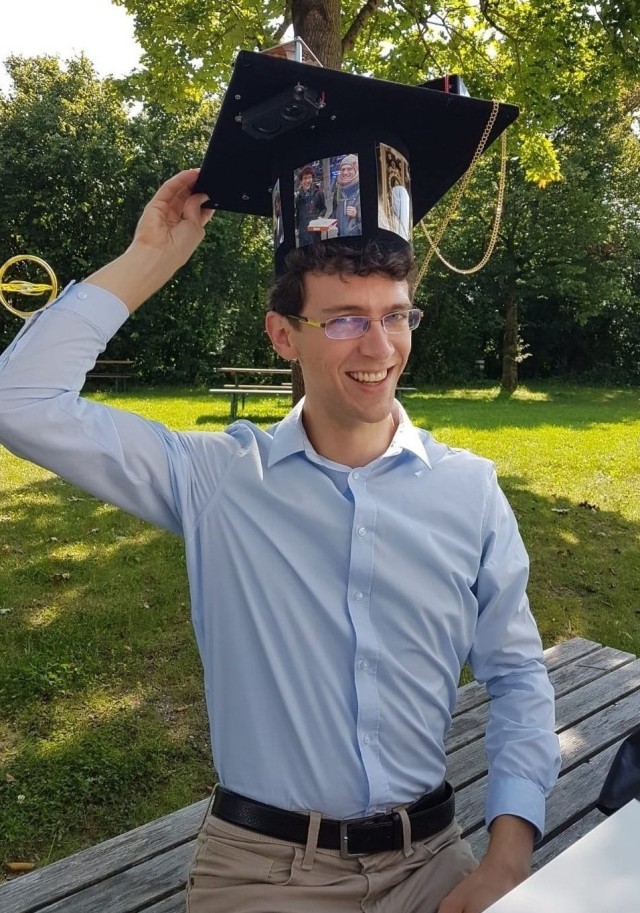 Benjamin Merkel sitting outdoors wearing his graduation cap.