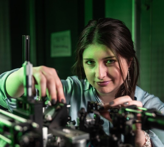 Viviana looks into the camera while working with an optical setup.