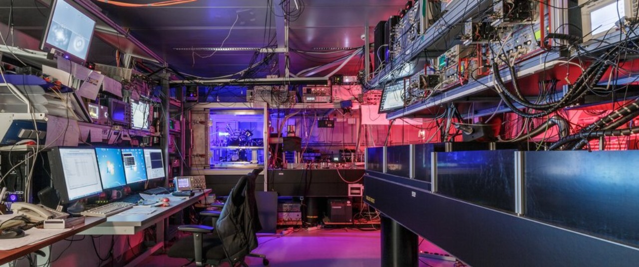 Experimental physics laboratory with computers and top tables featuring red and purple lights. 