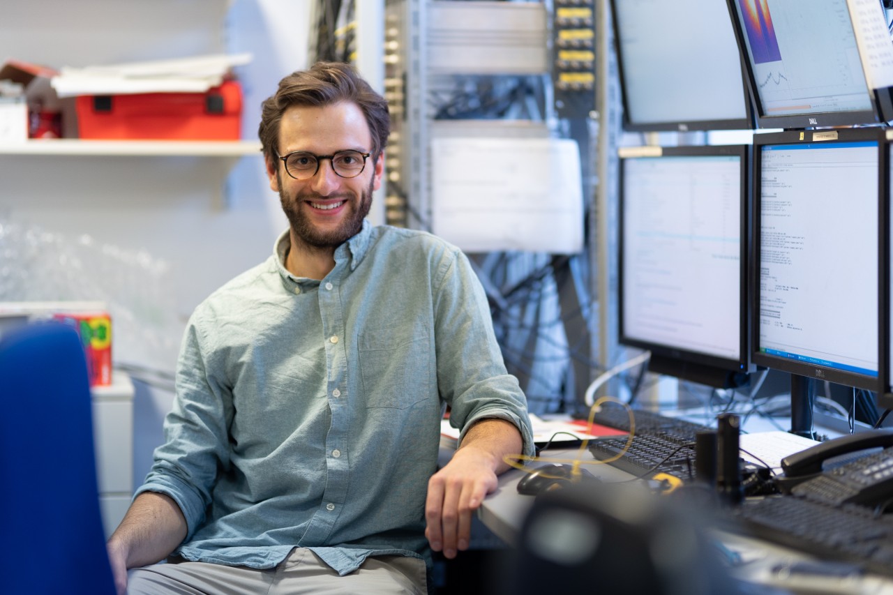 Christoph Braun sitting n front of a desk full of screens in his lab at LMU Munich. 