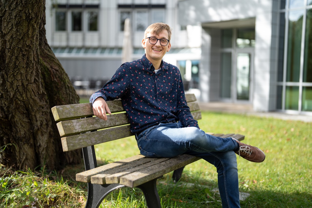 Man sitting on a bench, smilling, on a sunny day, in the MPQ garden.