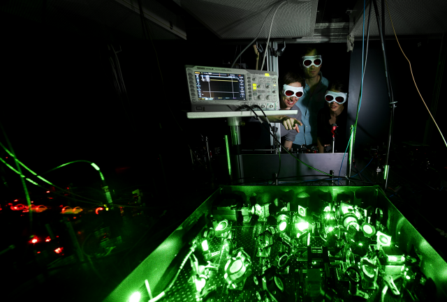 Summer Bachelor Program Students looking over a laser table wearing safety goggles.